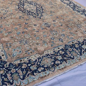 K&ouml;nnte beinhalten: Ein antiker Teppich mit einem beigefarbenen Mittelfeld und einem marineblauen Rand. Der Teppich weist komplizierte Blumenmuster in Blau-, Beige- und Hellgr&uuml;nt&ouml;nen auf. Das Design umfasst ein zentrales Medaillon und Eckakzente.