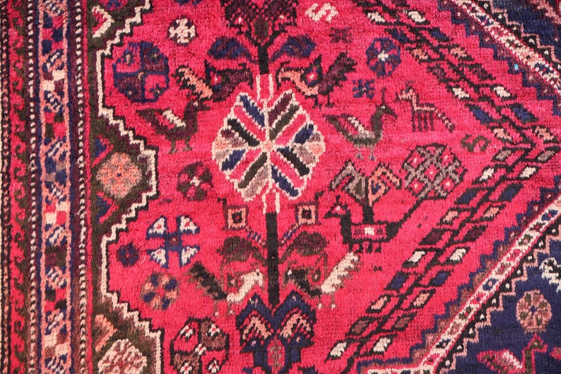 May include: Close-up of a vibrant red oriental rug with intricate patterns. The rug features a central floral design, stylized birds, and geometric borders in shades of blue, brown, and white. The rug's texture is visible.