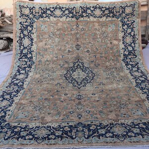 K&ouml;nnte beinhalten: Ein gro&szlig;er, rechteckiger Teppich mit einem komplizierten floralen Design. Der Teppich hat ein zentrales Feld in einem beigen Farbton, das von einem dunkelblauen Rand mit floralen Mustern umrahmt wird. Das Design des Teppichs umfasst blaue und hellblaue Akzente.