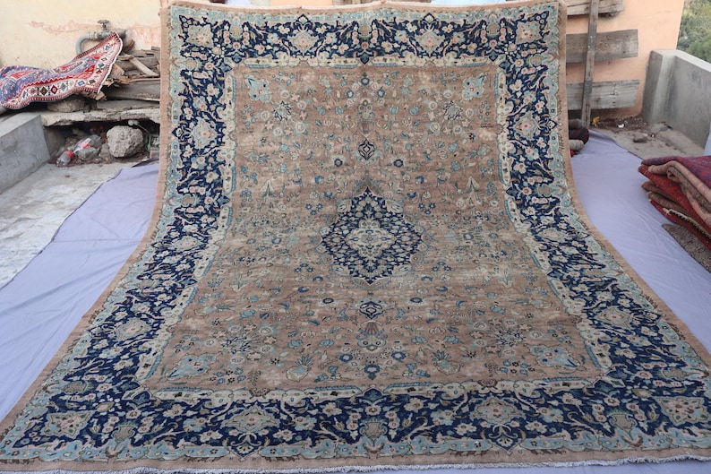 K&ouml;nnte beinhalten: Ein gro&szlig;er, rechteckiger Teppich mit einem komplizierten floralen Design. Der Teppich hat ein zentrales Feld in einem beigen Farbton, das von einem dunkelblauen Rand mit floralen Mustern umrahmt wird. Das Design des Teppichs umfasst blaue und hellblaue Akzente.