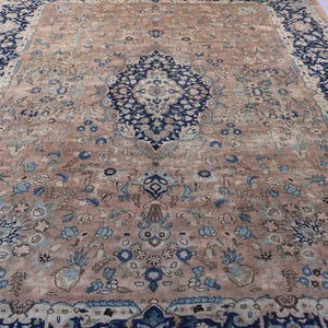 K&ouml;nnte beinhalten: Ein gro&szlig;er, rechteckiger Teppich mit einem komplizierten floralen Design. Der Teppich hat ein zentrales Medaillon in Marineblau, umgeben von einem Feld aus beige- und hellblauen Blumenmustern. Der Rand ist dunkelmarineblau mit floralen Motiven.
