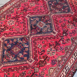 May include: A rectangular, hand-woven rug with a rich, red background and intricate geometric patterns in navy blue, brown, and cream. The rug features a central medallion design and a detailed border, showcasing traditional craftsmanship.