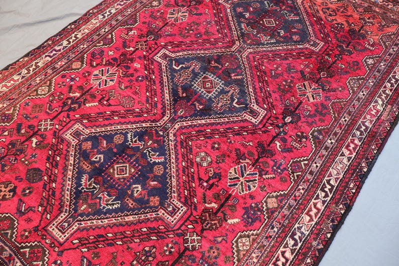 May include: A rectangular, hand-woven rug with a rich, red background and intricate geometric patterns in navy blue, brown, and cream. The rug features a central medallion design and a detailed border, showcasing traditional craftsmanship.