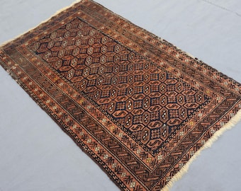 May include: Rectangular rug with a geometric pattern in shades of brown, black, and orange. The rug has a detailed design with a border and fringe on the ends. The rug's dimensions are not visible.
