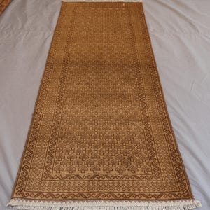 May include: A rectangular, brown rug with a repeating tree-like pattern and a decorative border. The rug has a fringe on both ends. The rug is made of a woven material.