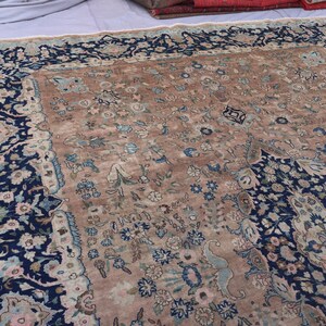 K&ouml;nnte beinhalten: Ein antiker persischer Teppich mit einem zentralen Feld in Beige und aufwendigen floralen Mustern in Blau-, Rosa- und Cremet&ouml;nen. Der Rand ist ein tiefes Marineblau mit floralen Motiven. Das Design des Teppichs ist symmetrisch und detailliert.