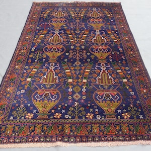 May include: A rectangular, hand-knotted rug with a deep blue field. The rug features a repeating pattern of stylized vases, trees, and floral motifs in shades of gold, red, green, and orange. The border is a complex design with similar colors.