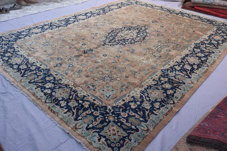 K&ouml;nnte beinhalten: Ein gro&szlig;er, rechteckiger Teppich mit einem aufwendigen floralen Design. Der Teppich hat ein zentrales Medaillon und einen Rand in den Farbt&ouml;nen Marineblau, T&uuml;rkis und Beige. Der Teppich ist wahrscheinlich aus Wolle und eignet sich f&uuml;r ein Wohn- oder Schlafzimmer.