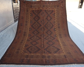 May include: A large rectangular area rug featuring a deep brown and dark chocolate color palette. The rug displays a repeating geometric pattern of diamonds and jagged lines throughout the center, framed by a wide border with small motifs.