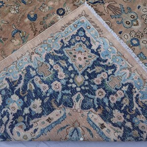 K&ouml;nnte beinhalten: Ein antiker Teppich mit detailliertem Blumenmuster. Der Teppich hat ein Mittelfeld in Braun- und Beiget&ouml;nen mit einem Rand in Marineblau und Hellblau. Das Design umfasst florale und botanische Motive mit einem Fransenrand.