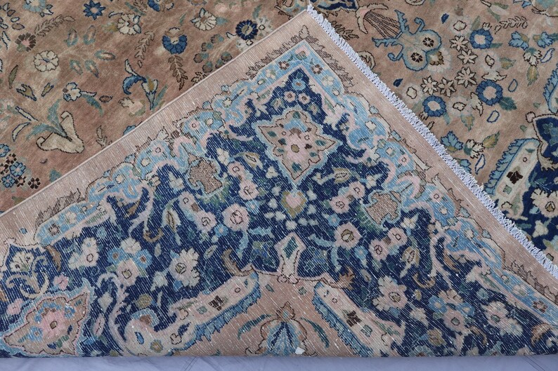 K&ouml;nnte beinhalten: Ein antiker Teppich mit detailliertem Blumenmuster. Der Teppich hat ein Mittelfeld in Braun- und Beiget&ouml;nen mit einem Rand in Marineblau und Hellblau. Das Design umfasst florale und botanische Motive mit einem Fransenrand.