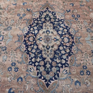 K&ouml;nnte beinhalten: Nahaufnahme eines Teppichs mit aufwendigem Blumenmuster. Der Teppich hat ein zentrales Medaillon in Marineblau und Creme, umgeben von einem beigen Feld und akzentuiert mit blauen und hellblauen Blumenmotiven.