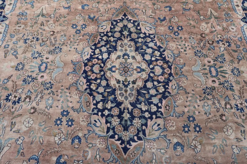K&ouml;nnte beinhalten: Nahaufnahme eines Teppichs mit aufwendigem Blumenmuster. Der Teppich hat ein zentrales Medaillon in Marineblau und Creme, umgeben von einem beigen Feld und akzentuiert mit blauen und hellblauen Blumenmotiven.