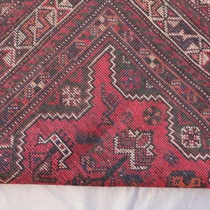 May include: Close-up of a section of a red, black, and white patterned rug. The rug features geometric designs and a fringed edge. The color palette includes deep reds, blacks, and off-white accents, creating a traditional aesthetic.