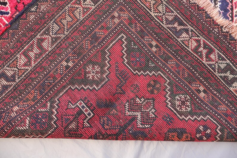 May include: Close-up of a section of a red, black, and white patterned rug. The rug features geometric designs and a fringed edge. The color palette includes deep reds, blacks, and off-white accents, creating a traditional aesthetic.