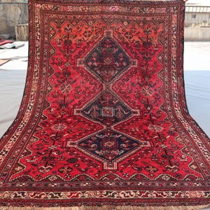 May include: A large, rectangular rug with a central diamond pattern in navy blue and red. The rug features intricate floral and geometric designs, with a fringed edge. The color palette includes shades of red, navy, and cream.