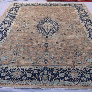 K&ouml;nnte beinhalten: Ein gro&szlig;er, rechteckiger Teppich mit einem komplizierten floralen Design. Der Teppich hat ein zentrales Medaillon und einen Rand in den Farbt&ouml;nen Marineblau, Beige und Hellblau. Der Teppich ist wahrscheinlich aus Wolle und eignet sich f&uuml;r ein Wohn- oder Schlafzimmer.