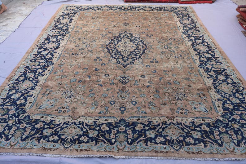 K&ouml;nnte beinhalten: Ein gro&szlig;er, rechteckiger Teppich mit einem komplizierten floralen Design. Der Teppich hat ein zentrales Medaillon und einen Rand in den Farbt&ouml;nen Marineblau, Beige und Hellblau. Der Teppich ist wahrscheinlich aus Wolle und eignet sich f&uuml;r ein Wohn- oder Schlafzimmer.