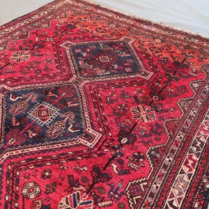 May include: A rectangular, hand-knotted rug with a central geometric design in deep red and navy blue. The rug features intricate patterns and a detailed border, showcasing a traditional aesthetic. The rug's color palette includes shades of red, blue, and cream.