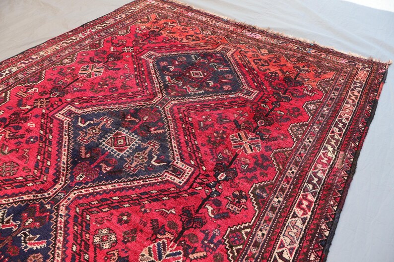 May include: A rectangular, hand-knotted rug with a central geometric design in deep red and navy blue. The rug features intricate patterns and a detailed border, showcasing a traditional aesthetic. The rug's color palette includes shades of red, blue, and cream.