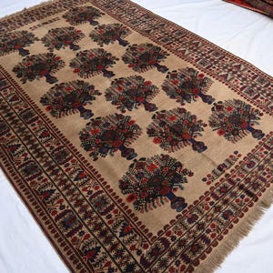 May include: Beige rectangular rug featuring a repeating pattern of stylised floral designs in red, brown, and blue. The rug has a detailed border and fringing along the edges, showcasing a traditional design.