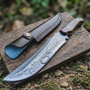 Könnte beinhalten: Ein Jagdmesser aus Damaststahl mit Holzgriff und Lederscheide. Die Klinge hat ein einzigartiges Muster und liegt auf einer Holzoberfläche. Die Scheide ist braun mit einem Knopfverschluss.