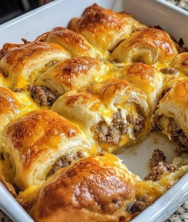 May include: A close-up shot of a baked casserole dish filled with golden-brown, flaky pastries. The pastries are stuffed with a savory meat filling and topped with melted cheese, creating a delicious and appetizing meal.