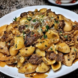 Peut inclure: Gros plan sur une assiette blanche remplie de coquillettes, garnies de morceaux de viande, de fromage fondu et de persil frais. Les pâtes sont nappées d'une sauce crémeuse, d'aspect riche et savoureux.