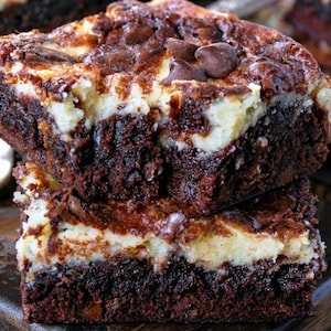 May include: Two stacked brownies with a creamy, light-coloured layer and dark chocolate chunks on top. The brownies are a rich, dark brown, suggesting a fudgy texture. A delicious treat.