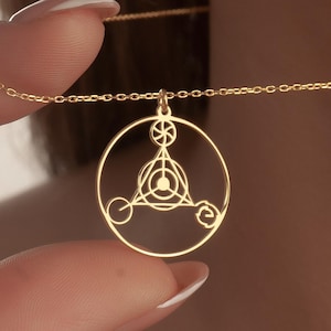 May include: A gold pendant necklace with a circular design and geometric shapes. The pendant is suspended from a fine chain. The necklace is held up by a person's fingers.