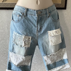 以下が含まれることがあります： 装飾パッチ付きのライトブルーデニムショーツ。 ショーツは、スパンコールとレースのディテールが施された、使い古されたパッチが特徴です。 花柄のボタンが付いた小さなポケットが見えます。 ショーツは裾が折り返されています。