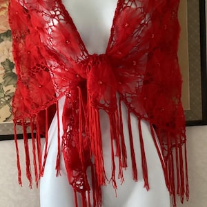 Könnte beinhalten: Ein roter Spitzenschal mit floralem Muster und Fransen. Der Schal ist über einer Schaufensterpuppe drapiert. Die rote Spitze ist mit kleinen Verzierungen versehen. Der Schal hat einen leuchtenden Rotton.