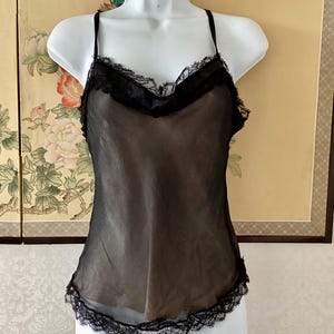 以下が含まれることがあります： Vネックラインと裾に繊細な黒のレーストリムがあしらわれた、透け感のある黒のキャミソール。細い調節可能なスパゲッティストラップが付いており、マネキンに着せた状態でフィット感のあるシルエットが特徴です。