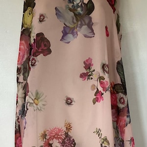 Könnte beinhalten: Ein ärmelloses, hellrosa Kleid mit einem lebendigen Blumenmuster. Das Kleid hat einen runden Ausschnitt und ist mit einer Mischung aus bunten Blumen bedeckt, darunter Rosen, Iris und Gänseblümchen, was einen femininen und eleganten Look erzeugt.