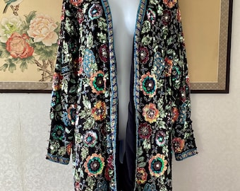 May include: A black open-front jacket featuring intricate floral embroidery with multicolored sequins and beads. The garment has long sleeves, a straight hem, and a decorative teal beaded trim along the front opening, cuffs, and bottom edge.