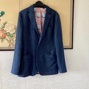 May include: A dark blue blazer with a textured finish, featuring a notched lapel, two front buttons, and two side pockets. The interior lining is a light pink fabric decorated with a pattern of large, circular, light blue and white polka dots.