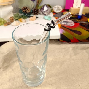 May include: A clear glass drinking straw with a black silicone wrap around the middle. The straw is in a clear glass with a textured surface.