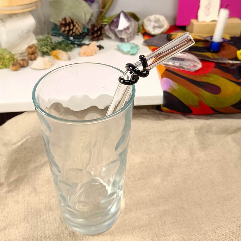 May include: A clear glass drinking straw with a black silicone wrap around the middle. The straw is in a clear glass with a textured surface.