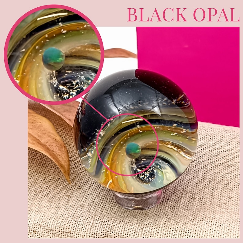 Pode incluir: Um peso de papel de vidro de opala preta com um design de gal&aacute;xia em espiral. O peso de papel apresenta um orbe verde no centro da gal&aacute;xia.