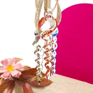 May include: Three glass ornaments in the shape of a spiral, each with a different colour gradient. The ornaments are suspended from a twine string.