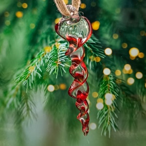 May include: A red and clear glass Christmas bauble shaped like a candy cane. The bauble is hanging from a string.