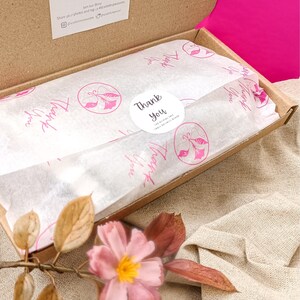May include: A brown cardboard box with a white tissue paper lining. The tissue paper has a pink floral pattern and the words "Thank You" printed on it. The box is open and the tissue paper is folded over the top.