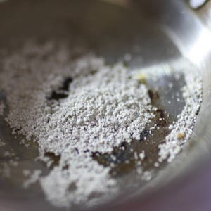 Pode incluir: Um close-up de uma panela de fritar de prata com res&iacute;duos de p&oacute; branco no fundo.