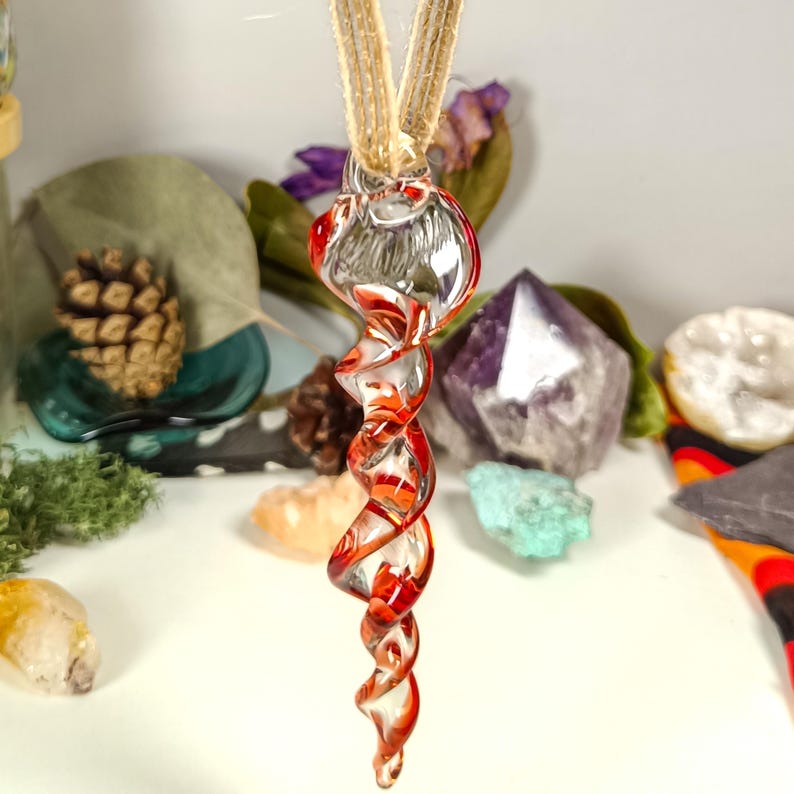 May include: A glass pendant with a spiral design in red and clear glass. The pendant is hanging from a brown cord.