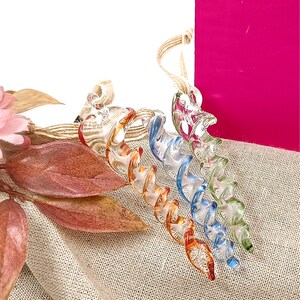 May include: A set of five glass baubles in a spiral shape. The baubles are in shades of orange, blue, green, and clear. The baubles are hanging from a twine string.
