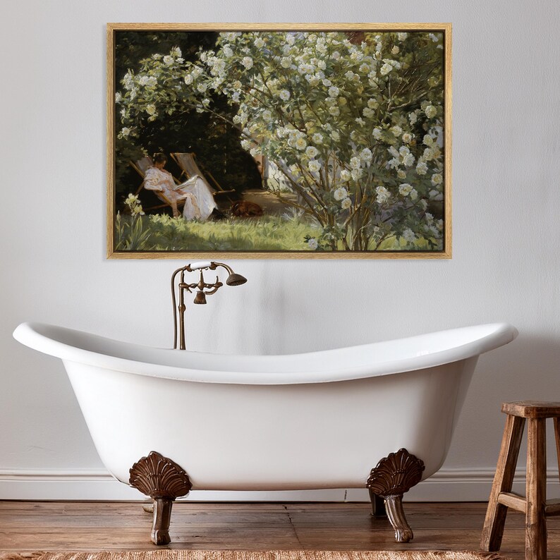May include: A framed painting depicts a woman in a white dress relaxing in a garden, surrounded by white flowers. The painting hangs above a white clawfoot bathtub with bronze fixtures and a wooden stool.