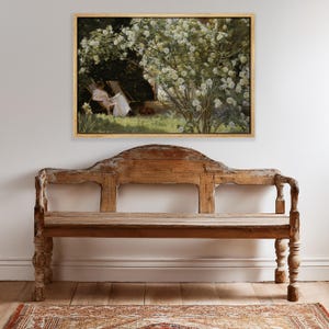 May include: A framed painting depicts a woman in a white dress relaxing in a garden, beneath a flowering tree. The painting hangs above a weathered wooden bench with a curved back. A patterned rug is visible on the wooden floor.