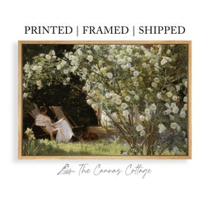 May include: A framed print of a vintage garden scene. The artwork depicts a person relaxing in a chair under a blooming white rose bush. The text at the top reads "PRINTED | FRAMED | SHIPPED". The Canvas Cottage logo is at the bottom.