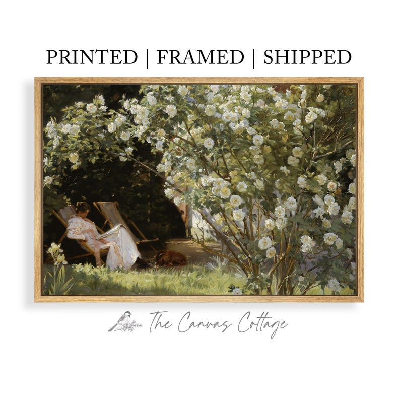 May include: A framed print of a vintage garden scene. The artwork depicts a person relaxing in a chair under a blooming white rose bush. The text at the top reads "PRINTED | FRAMED | SHIPPED". The Canvas Cottage logo is at the bottom.