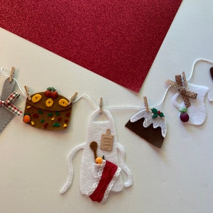 Könnte beinhalten: Eine Weihnachtsgirlande aus Filz mit verschiedenen festlichen Dekorationen, darunter ein Pizzastück, ein Kuchen, ein Krug, ein Pudding und eine Schürze. Die Girlande ist mit weißem Garn aufgefädelt und hat Holz-Wäscheklammern, die jede Dekoration halten.